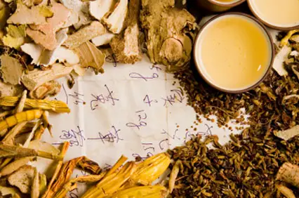 Chinese herbal medicine ingredients arranged around a handwritten prescription and tea