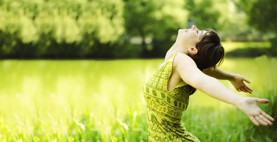 Woman stretching her arms wide in a sunlit green park, feeling free of pain